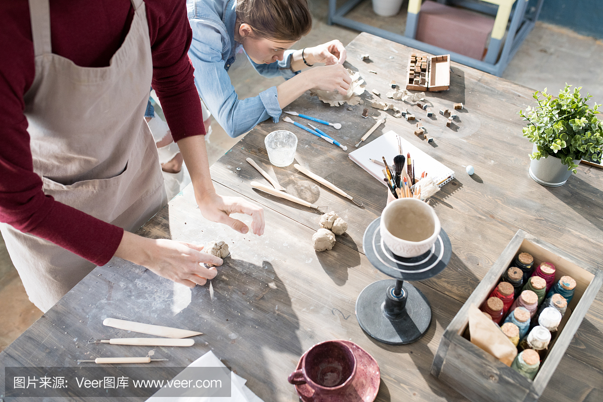 肮脏的木桌,陶工在车间里用粘土和模具制作手工杯子